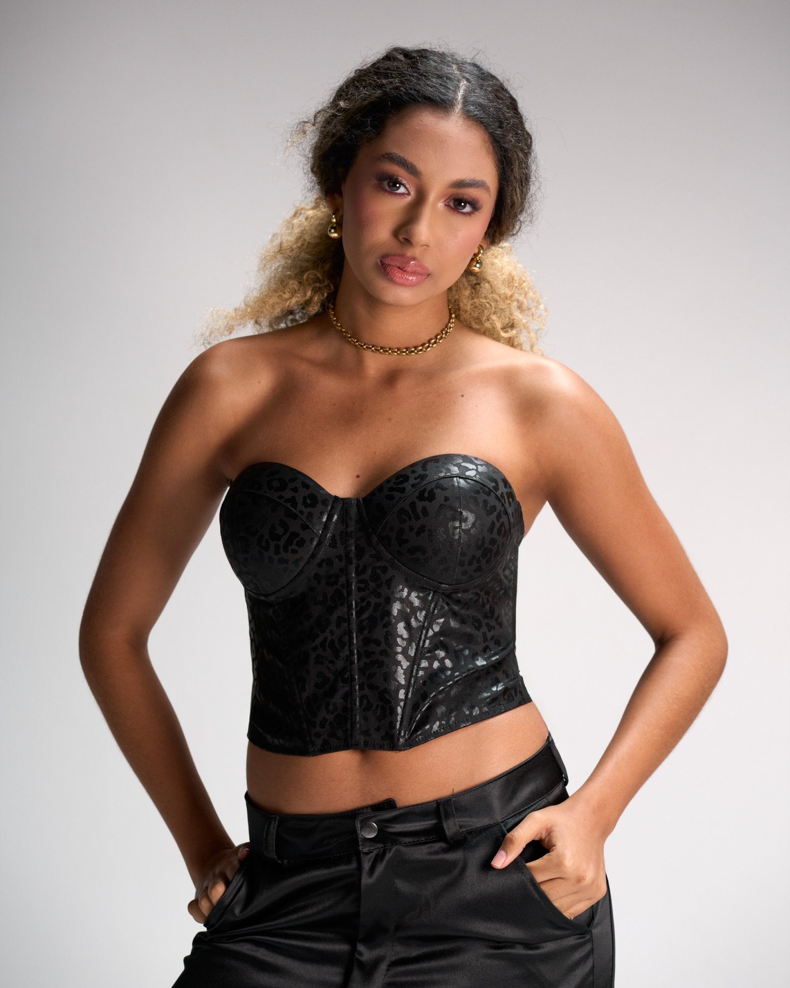 Bold leopard print leather bustier top with cut-out detail, paired with black satin pants, showcasing edgy fashion style for modern women.