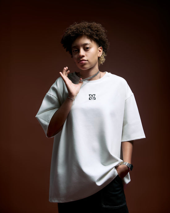 Fashion-forward young woman with modern style and confident pose, wearing a casual oversized white t-shirt with logo, layered jewelry, and stylish accessories.