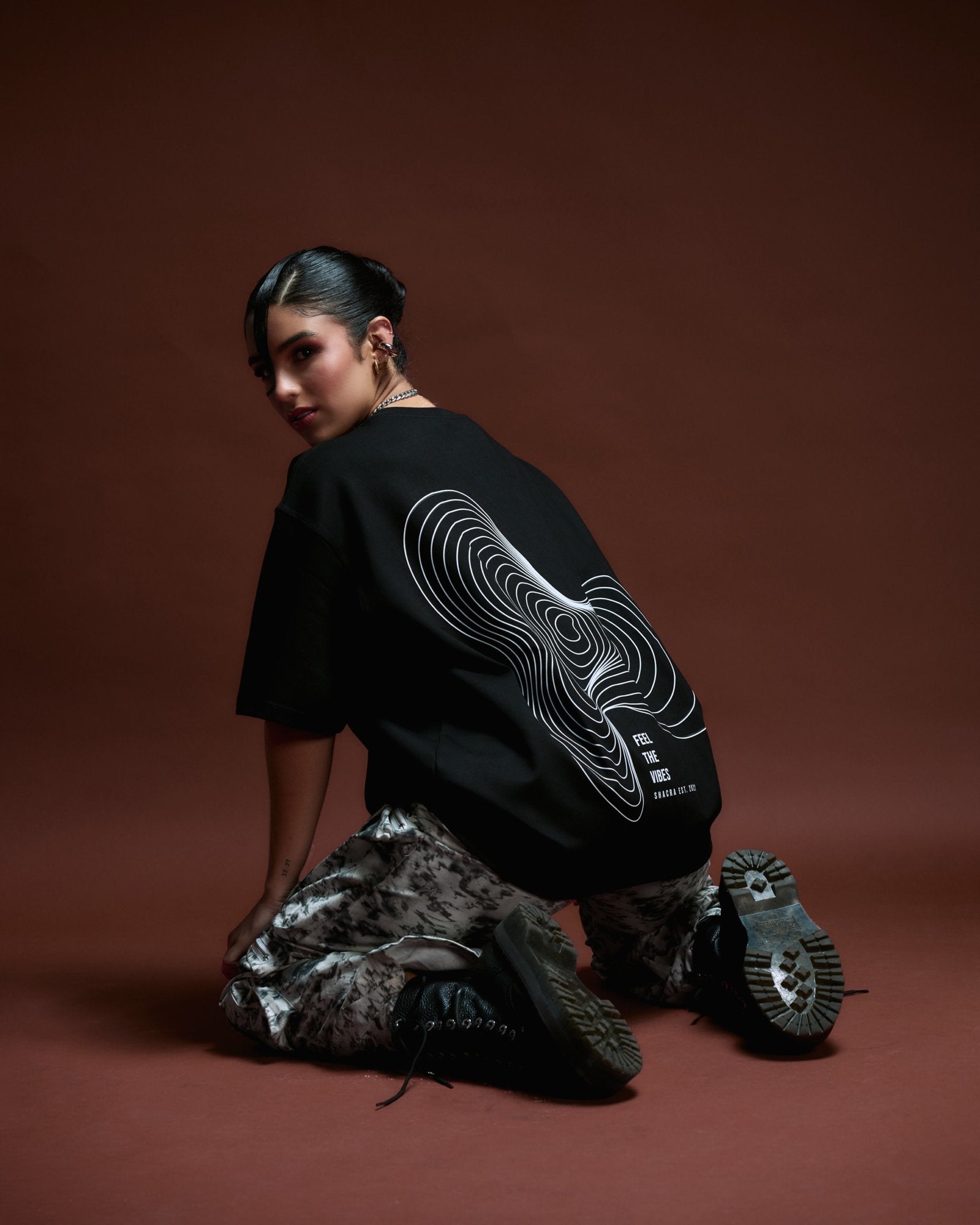 Contemporary fashion model wearing urban streetwear with graphic print, black oversized t-shirt and camouflage pants, showcasing bold style and modern aesthetics for fashion-forward individuals.