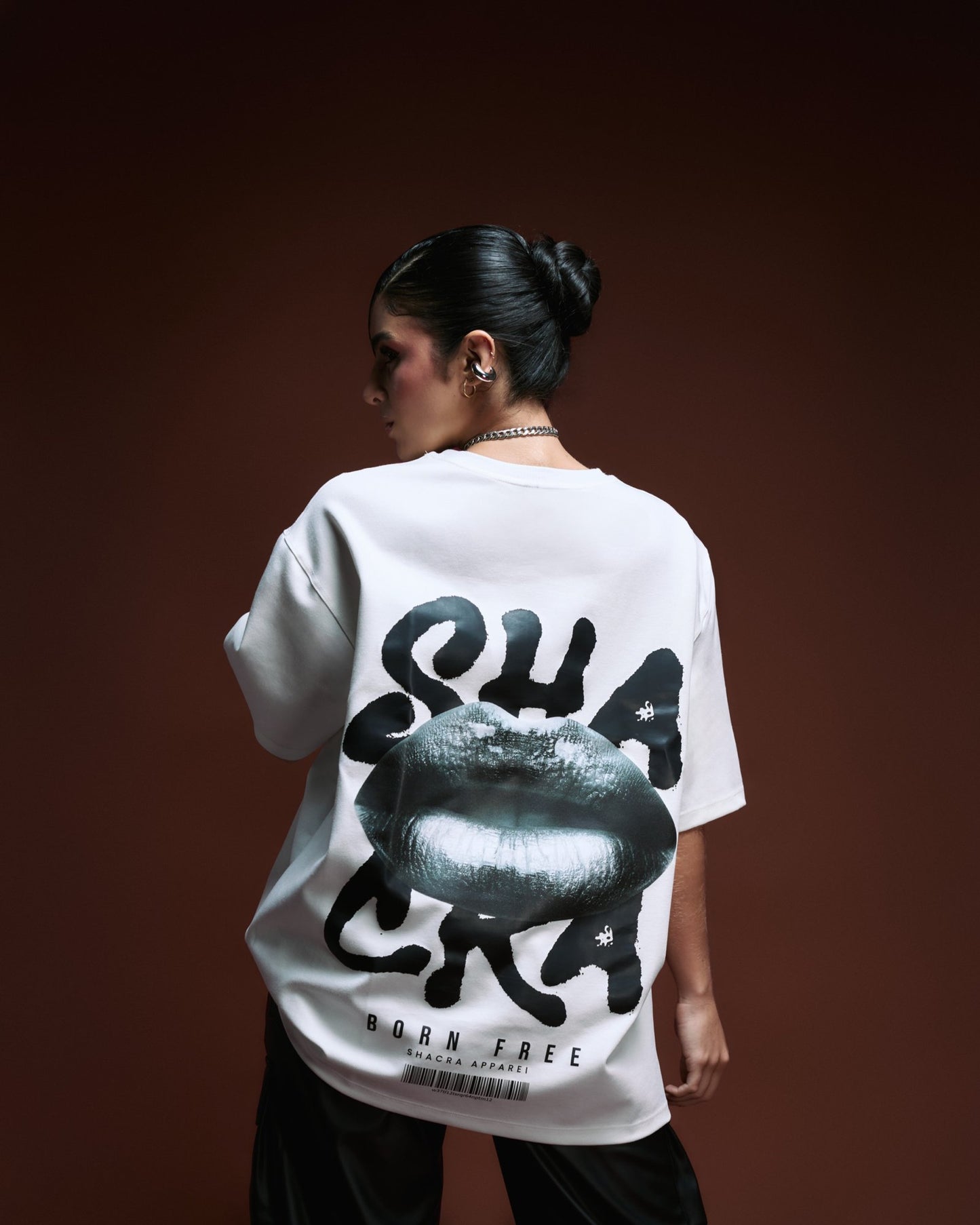 Stylish woman modeling a graphic oversized T-shirt with lips print and bold text, highlighting modern streetwear fashion from Shacra Apparel against a dark gradient background.