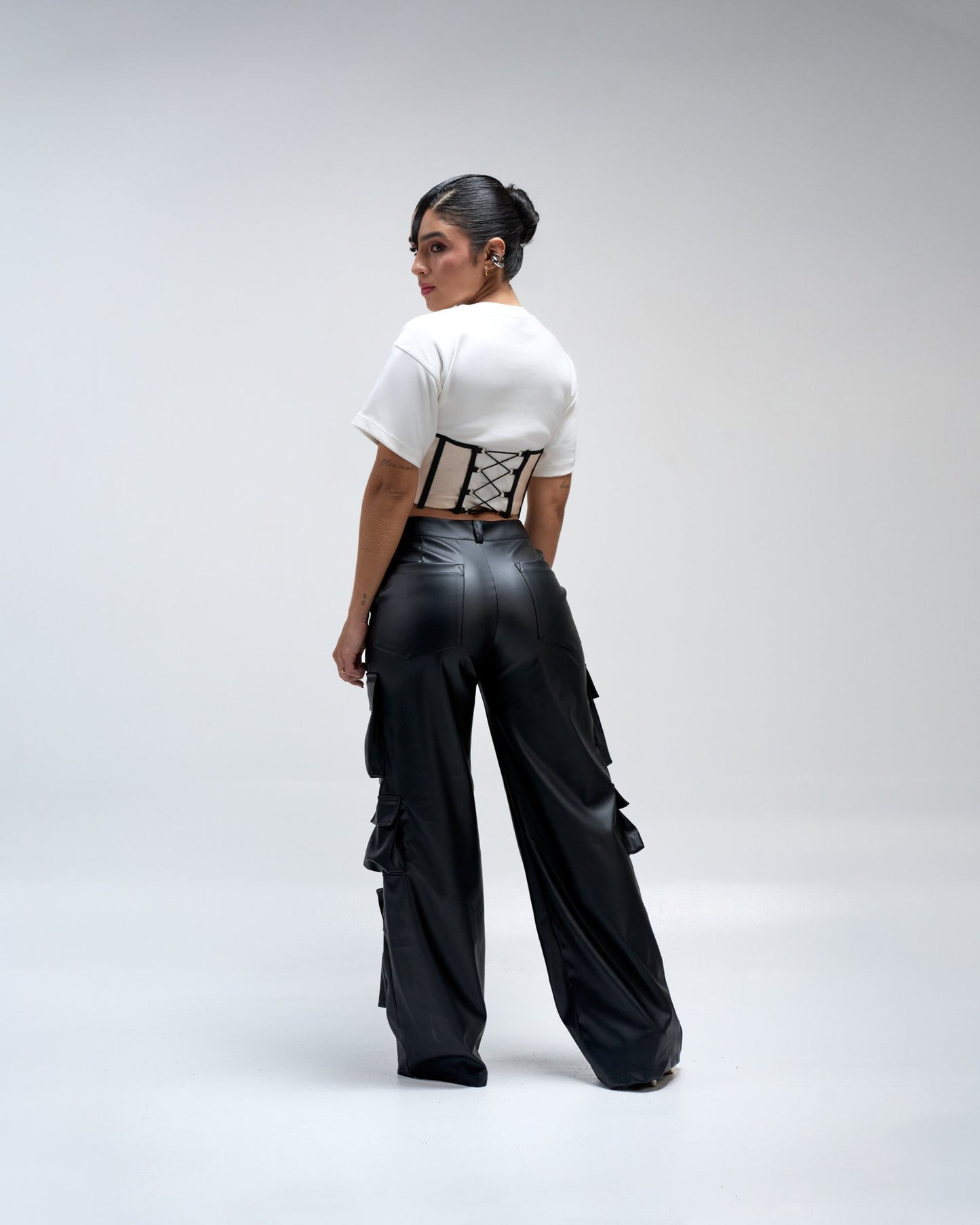 Bold fashion model wearing black leather wide-leg pants and a white cropped T-shirt with lace-up corset detail, showcasing edgy style and contemporary streetwear fashion.