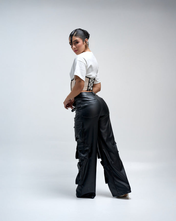 Stylish woman modeling black leather cargo pants and white cropped t-shirt against a plain light gray background, showcasing trendy fashion, urban streetwear, and modern clothing styles.