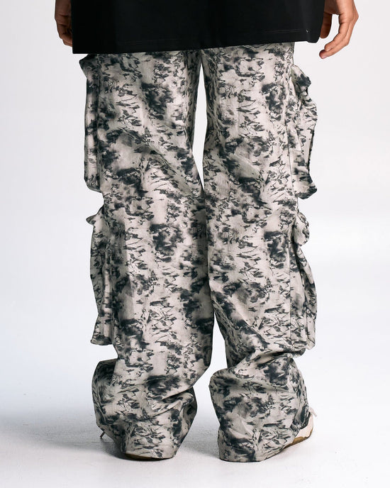 Baggy cargo pants with a black, white, and gray abstract print, featuring multiple pockets and ruffle details on the sides, styled for a fashion-forward streetwear look.