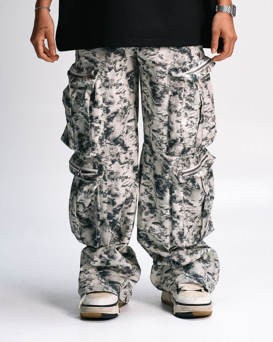 Cargo jogger pants with a black and white marble print, zippers, and a relaxed fit, styled for streetwear fashion, seen on a model wearing stylish sneakers, showcasing trendy urban apparel.