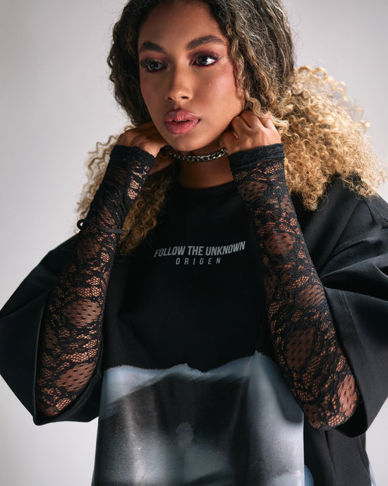 Elegant woman wearing black lace arm warmers and a graphic T-shirt with the text "Follow the Unknown" for stylish streetwear fashion.