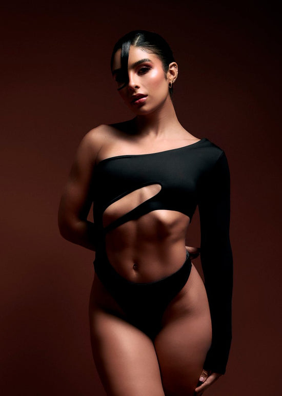 Striking woman with sculpted abs in edgy black cut-out outfit, dark background, high fashion, fitness, empowerment, beauty, body positivity, fashion photography, modern style, confident pose.