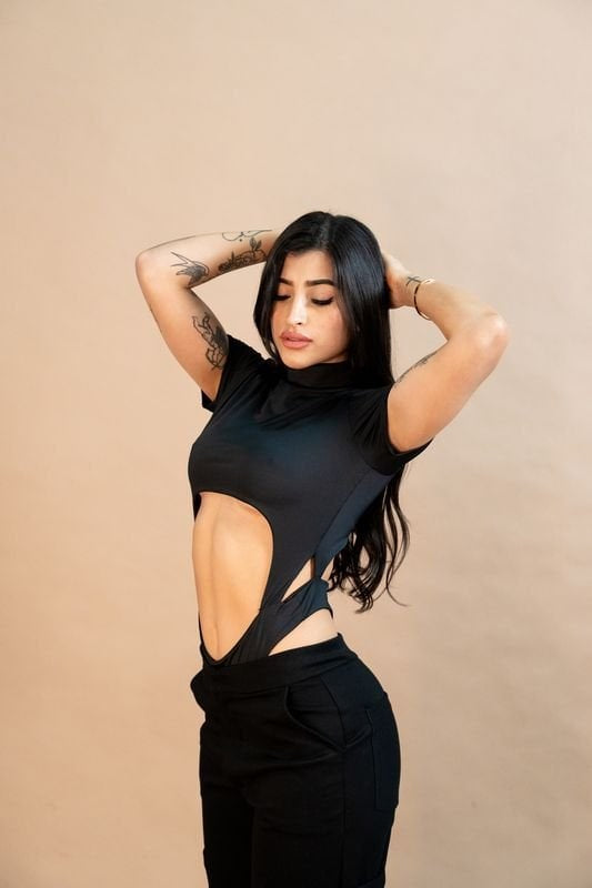 Vegan leather cut-out bodysuit with a sleek black finish, emphasizing modern fashion and body positivity. Perfect for stylish outfits and contemporary wardrobe essentials.