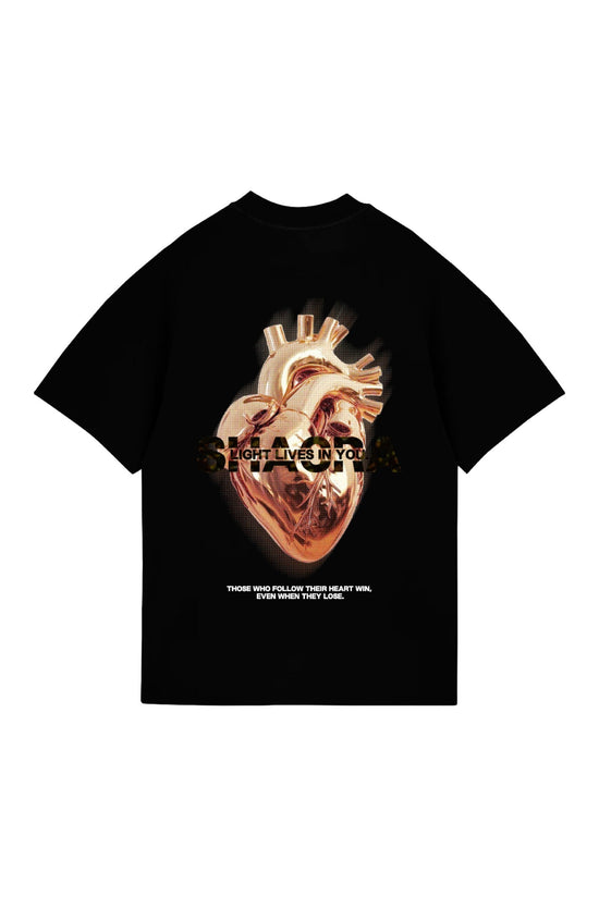 Vibrant black T-shirt featuring a detailed, artistic depiction of a human heart with metallic finish, accompanied by the phrase "Light lives in you" and inspiring quote about following one's heart.