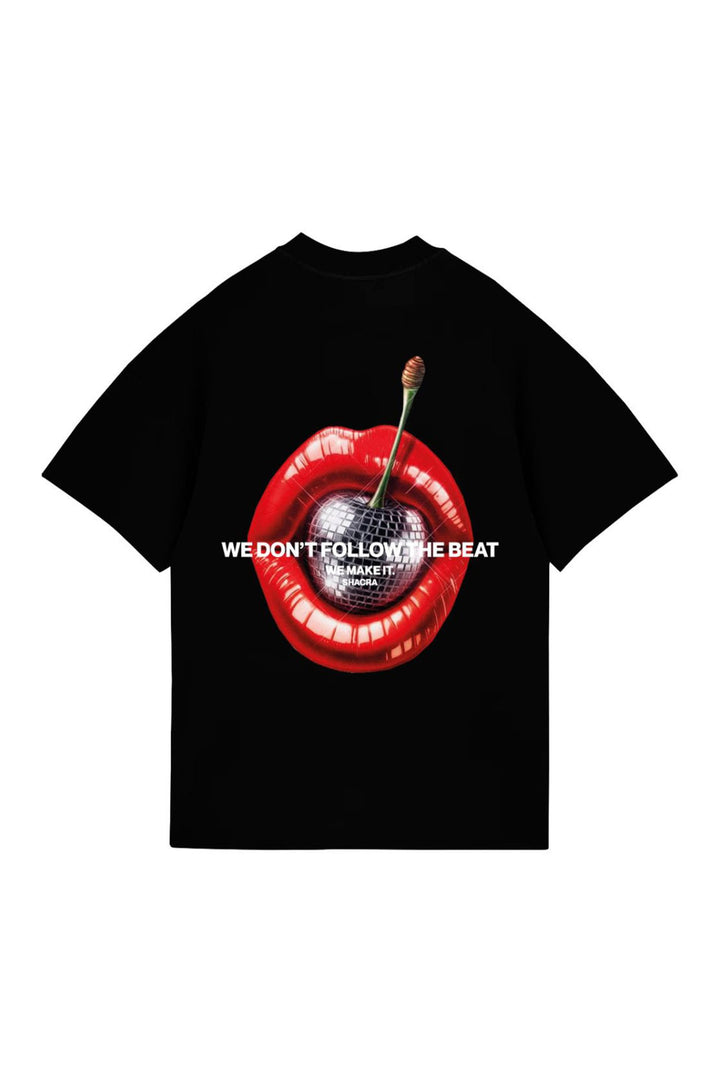 Vivid black T-shirt featuring a bold graphic of red lips with a cherry inside and a disco ball, emblazoned with the phrase "We don't follow the beat, we make it" for a statement-making fashion statement.